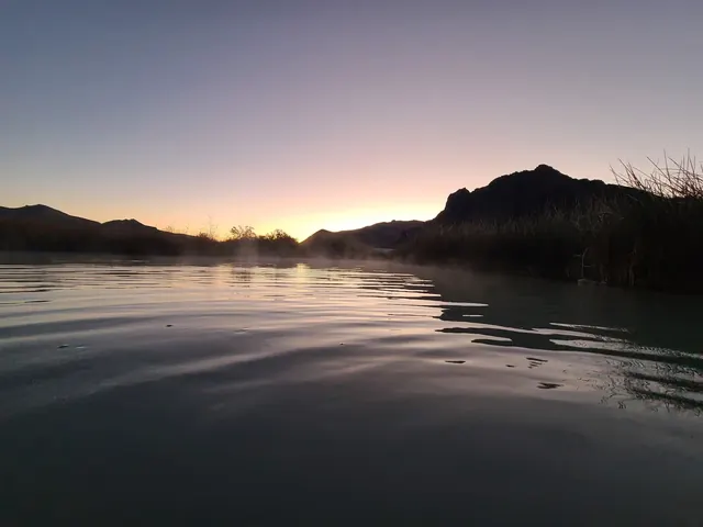 Twilight view of Black Rock Hot Springs pool with rising steam and silhouetted mountain landscape near Gerlach, Nevada