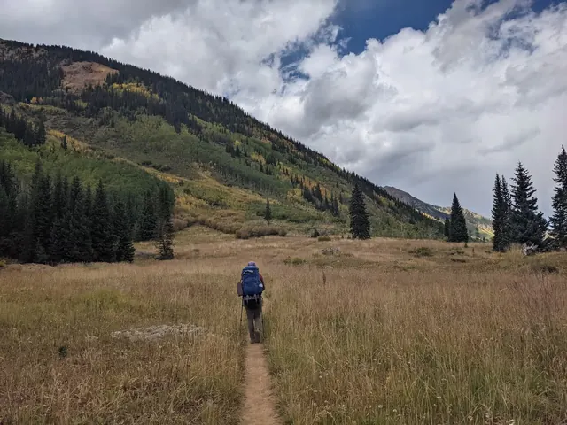 Hiker walking on trail through meadow with mountains in the distance near Conundrum Hot Springs, Aspen, Colorado.