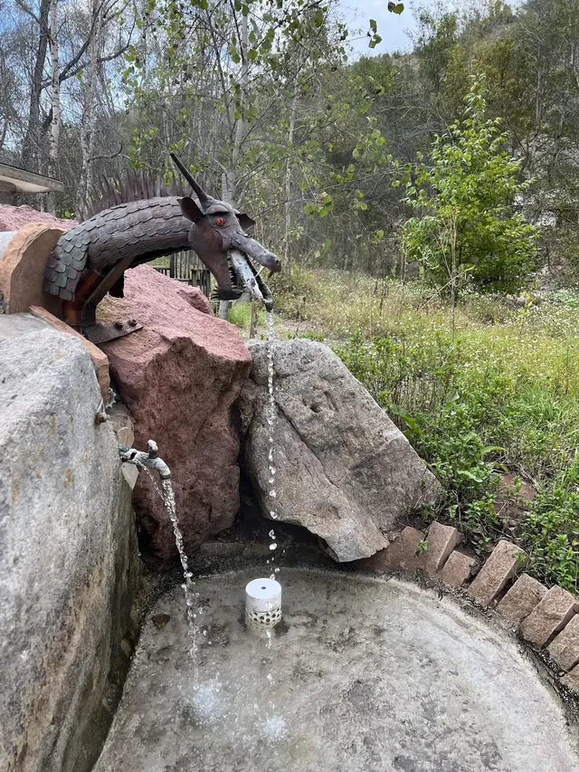 Metal dragon sculpture water spout pouring water into a rocky basin in a wooded area at Gila Hot Springs Campground in New Mexico.