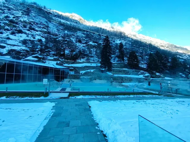 Steaming hot spring pools surrounded by snow-covered ground at Thermalbad Brigerbad with pine trees and mountains in Brig Switzerland.