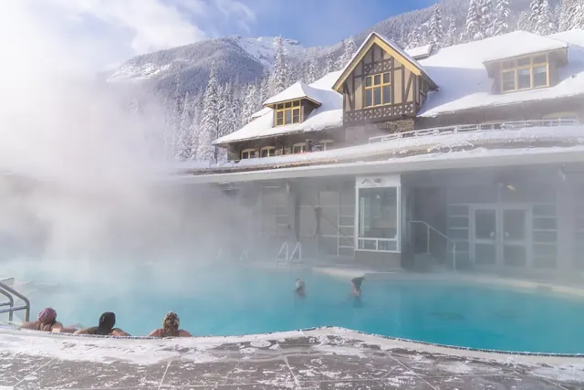 Outdoor hot spring pool with steam rising and people soaking in front of bathhouse at Banff Upper Hot Springs