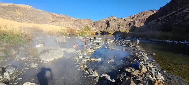 Multiple hot spring pools at Snively Hot Springs with people relaxing in sunny, rocky desert landscape near Adrian, Idaho, United States.