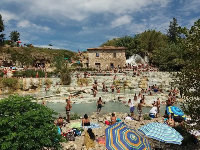 Crowded natural hot spring pools with visitors relaxing on terraces below a stone building at Cascate del Mulino in Saturnia.