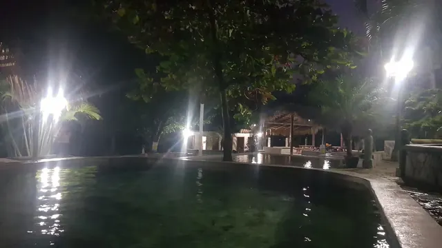 Large round hot spring soaking pool illuminated by several lights showing clear water and nearby leafy trees at Banos Termales El Brasilar.