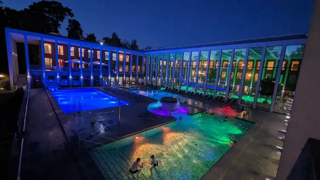 Nighttime view of outdoor pools at SaarowTherme with colorful underwater lights illuminating the water and people relaxing in Bad Saarow.