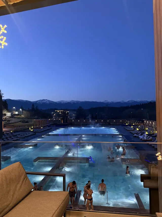 Steaming outdoor hot spring pools at dusk with people relaxing and mountain silhouettes in the distance near Banya, Bulgaria.