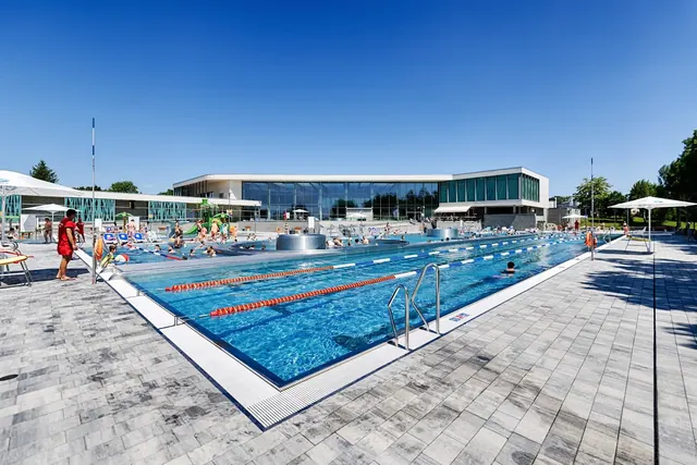 Large outdoor swimming pool with lanes and people relaxing near the glass-walled building of Termy Poddebice, Poland.