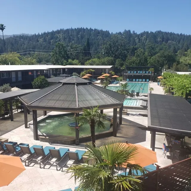 Covered circular hot spring pool surrounded by palm trees and orange umbrellas at Calistoga Spa Hot Springs in Calistoga California.
