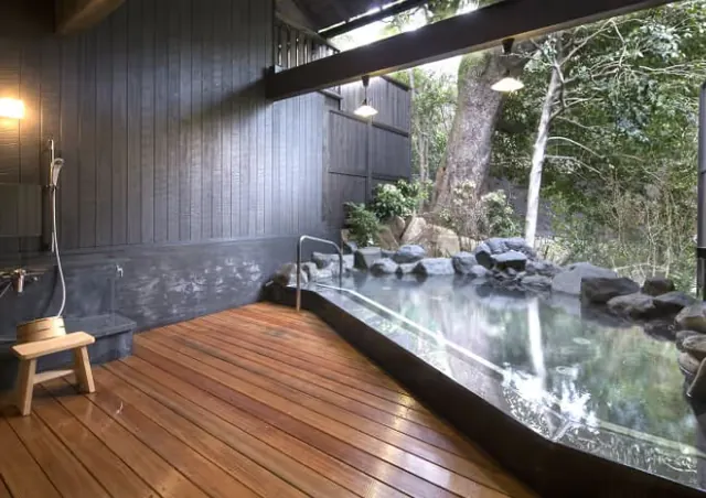 Indoor-outdoor hot spring pool with wooden floor and rock border under open roof at Hakone Yuryo in Hakone, Japan.