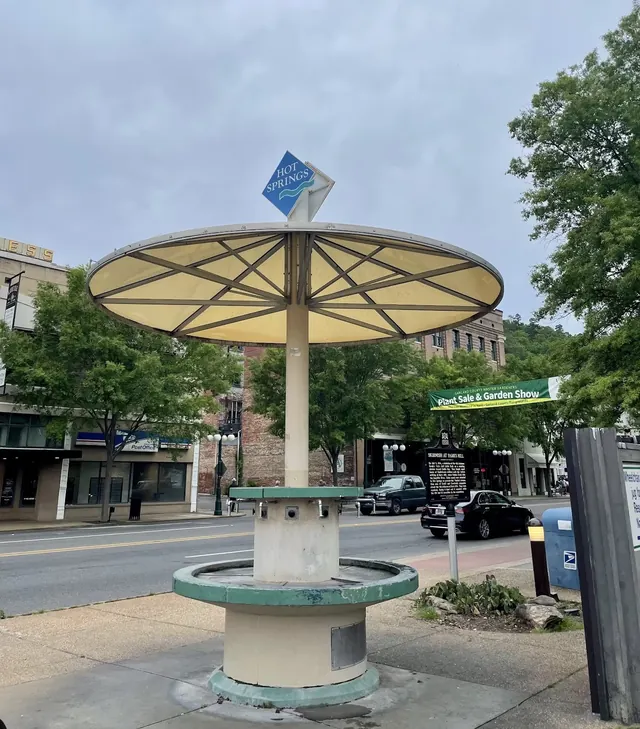 Outdoor concrete hot spring fountain with a large round canopy and blue hot springs sign in downtown Hot Springs, Arkansas.