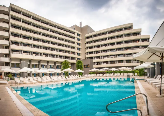 Large outdoor mineral pool surrounded by white umbrellas and lounge chairs with a modern hotel building at Interhotel Sandanski Thermal Poo.