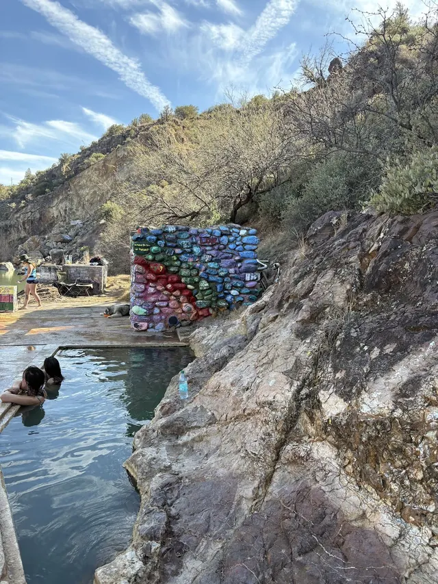 Several people relaxing in an outdoor hot spring pool at Verde Hot Springs, Arizona surrounded by rocky hills and painted rocks.