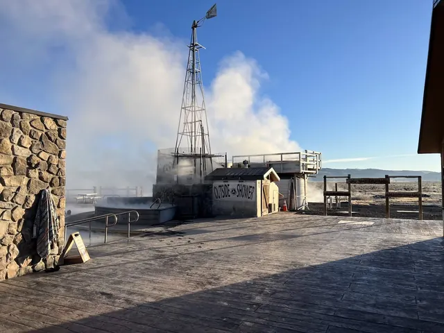 Steam rising from mineral soaking pools with windmill structure and outside shower area at Crystal Crane Hot Springs in Oregon.
