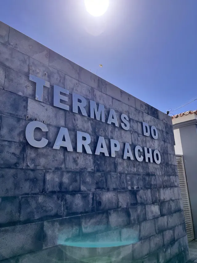 Stone-paved patio with two flagpoles, white wall, and ocean view near rocky islets at Termas do Carapacho in Santa Cruz da Graciosa Portuga.