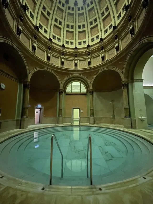 Circular indoor mineral pool with steps and columns under a domed ceiling with intricate artwork at Friedrichsbad hot spring in Germany.