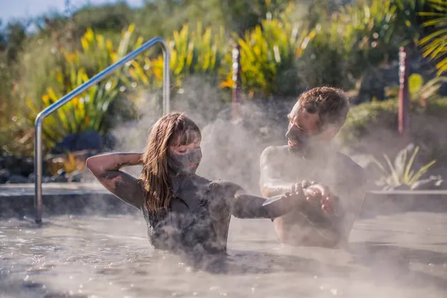 A man and woman covered in mud relax in a steaming hot spring pool at Hell's Gate Mud Bath & Spas in Rotorua New Zealand.