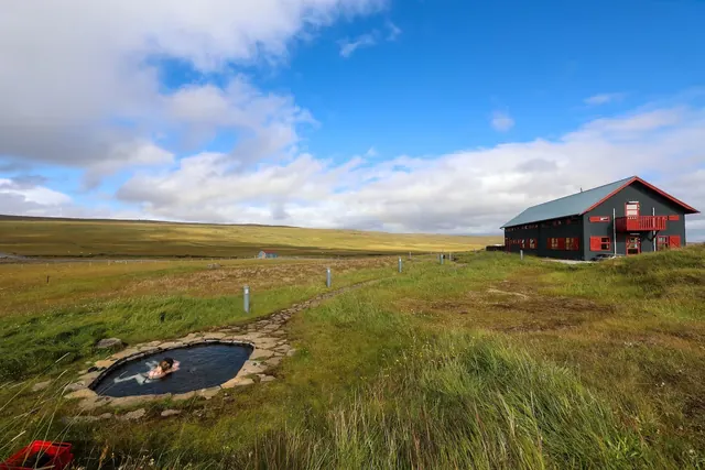 Single person enjoying the outdoor hot spring pool at Laugarfell Hot Springs with a wide grassy landscape and partly cloudy sky in Iceland.