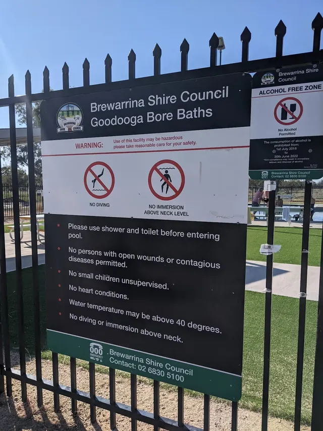 Black metal fence surrounding the Great Artesian Bore Baths facility in Goodooga NSW Australia with a sign listing safety rules and usage w.