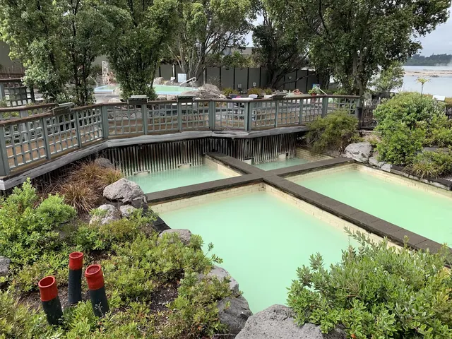 Four square outdoor mineral pools with light green water at Polynesian Spa in Rotorua New Zealand surrounded by trees and boardwalk.