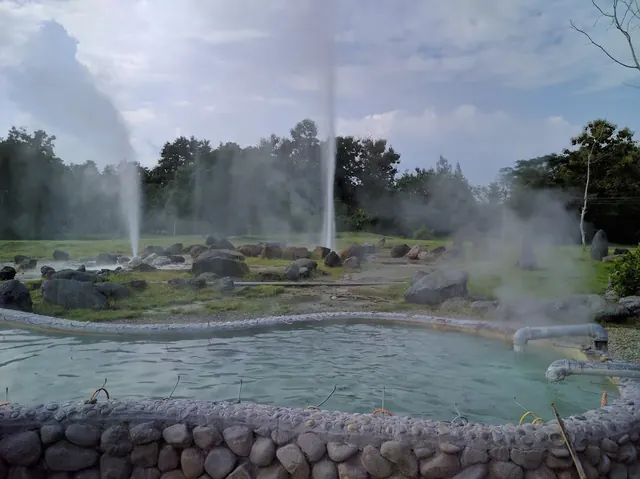 Several geysers releasing steam around a mineral water pool with stones at San Kamphaeng Hot Springs in Nan, Thailand.