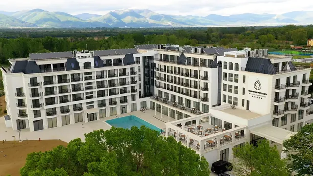 Aerial view of a multi-story white building surrounded by trees and mountains near Pavel Banya Bulgaria, part of the Grand Resort Pavel Ban.