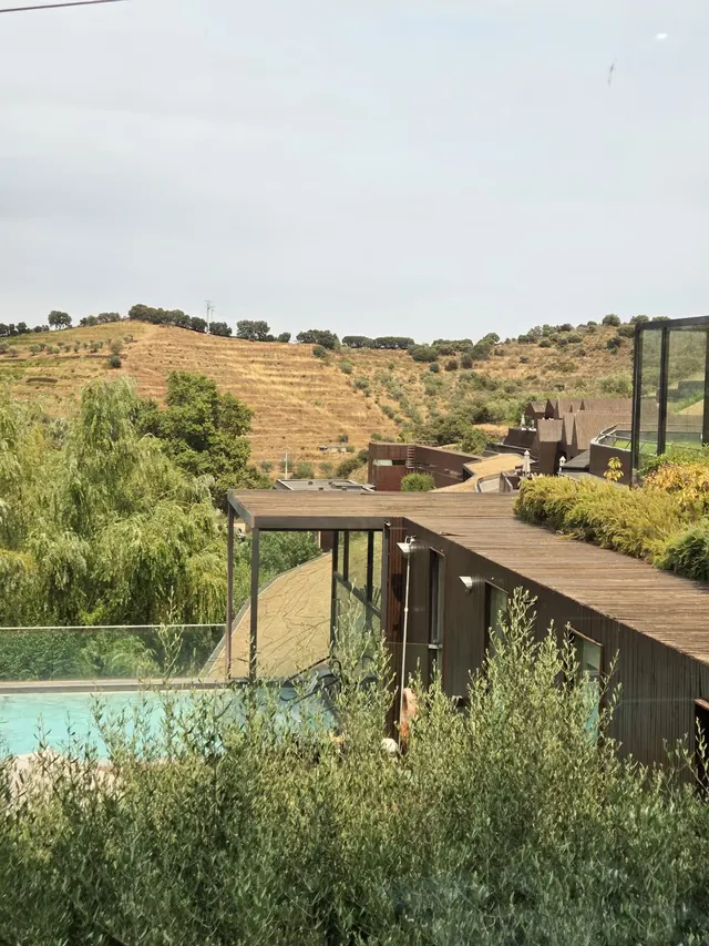 Clear water in an outdoor hot spring pool at Termas de Longroiva with wooden deck and rolling hills visible beyond shrubs.