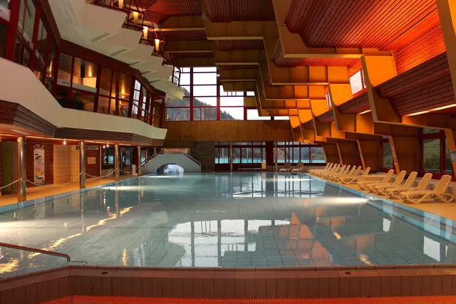 Indoor hot spring pool at Leukerbad Therme with rows of empty lounge chairs and warm wood paneling on the ceiling in Leukerbad Switzerland.