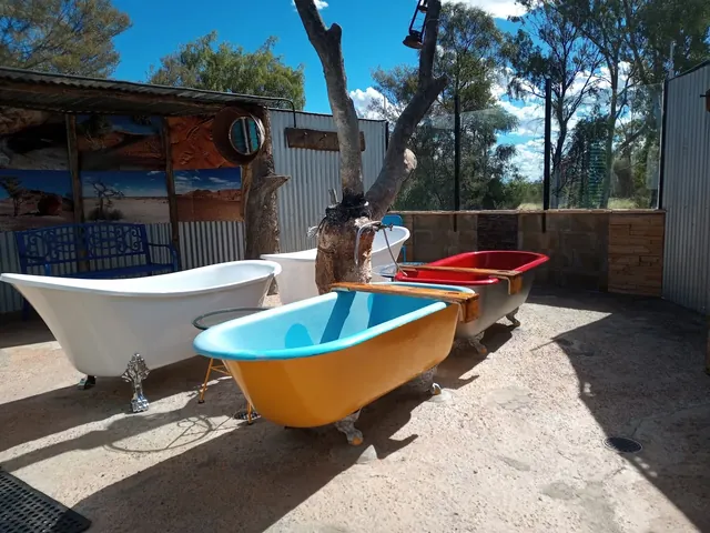 Outdoor area with several empty colorful clawfoot tubs and corrugated metal walls under a clear blue sky at Eulo Artesian Mud Baths.