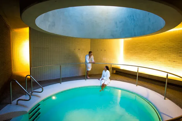 Round tiled hot spring pool under a circular skylight with two people in white robes chatting at Hepburn Bathhouse & Spa in Hepburn Springs.