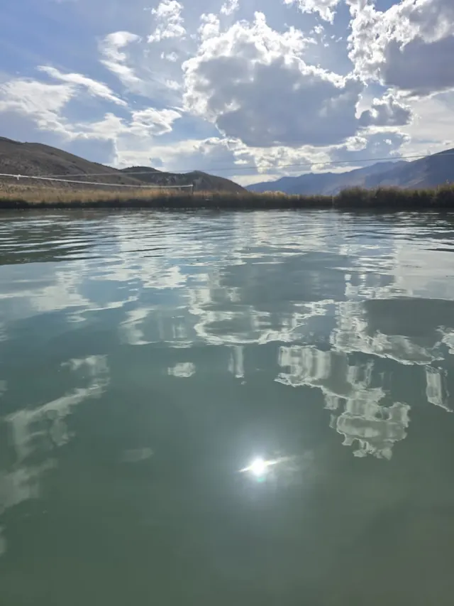 Close-up of water surface at Ruby Valley Hot Springs with reflections of clouds and sun, located near Elko, Nevada