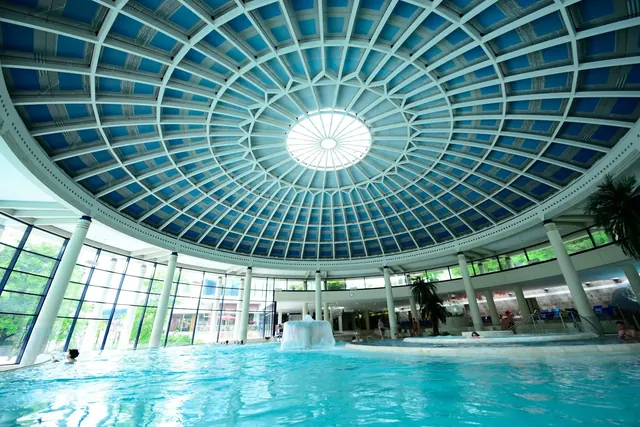 Indoor soaking pool at Caracalla Therme with clear blue water under a large skylight dome and pillars around the area.
