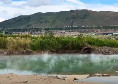 Steaming outdoor hot spring pool at Mountain Point Lake with green grasses and hills near Bluffdale, Utah.