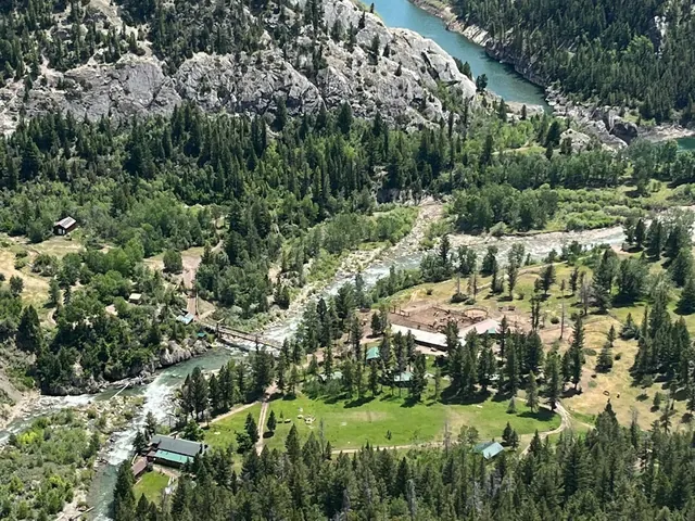 Aerial view of K Bar L Ranch hot spring ranch area showing river flowing through green forested valley with mountain rocks nearby in Montan.