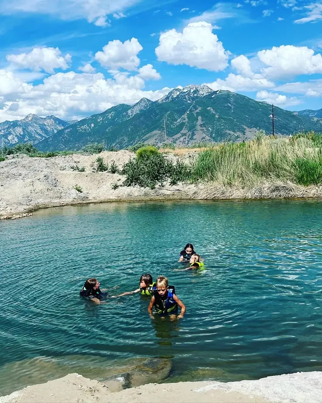 Several children wearing life jackets swimming in a natural pool at Mountain Point Lake with a mountain backdrop in Utah.