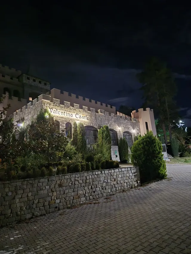 Stone castle building with Valentina Castle sign illuminated at night nestled among pine trees near Ognyanovo Bulgaria.