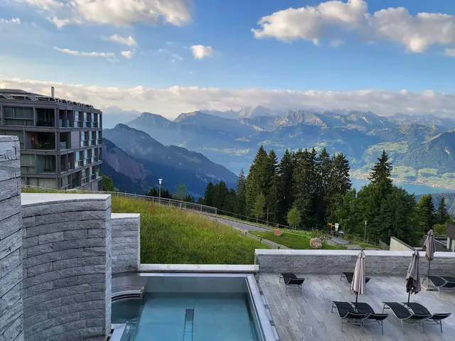 Outdoor soaking pool and stone patio overlooking mountains and trees at Mineralbad & Spa Rigi Kaltbad near Rigi Kaltbad, Switzerland.