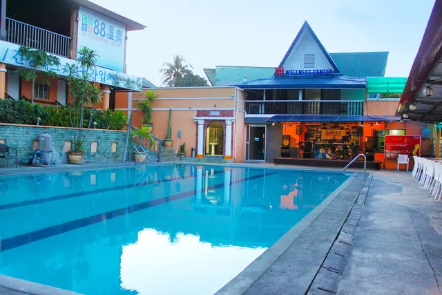 Calm outdoor pool at 88 Hot Spring Resort reflecting buildings with signage and vegetation, creating a serene atmosphere in Calamba City.