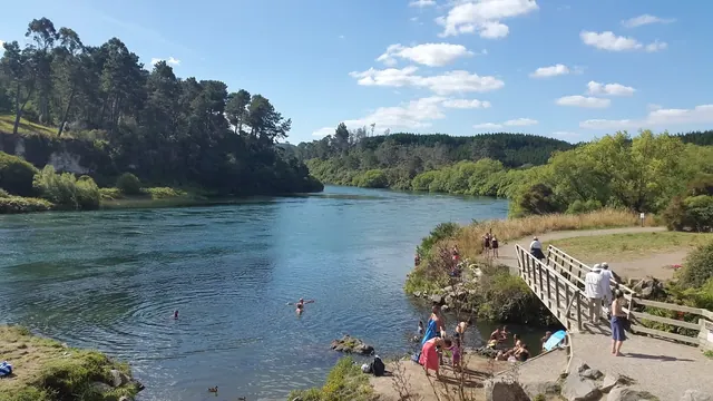 Outdoor river scene with a hot spring soaking area created by rocks where several people are enjoying the water under a clear sky near Taup.