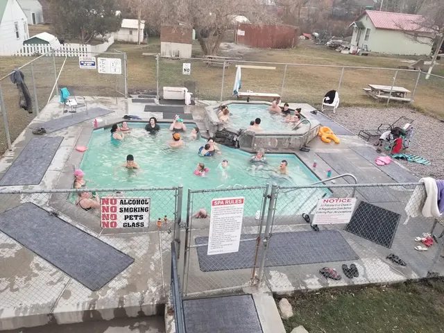 Crowded mineral pools with people relaxing in the water behind a chain link fence at Symes Hot Springs Hotel in Montana.