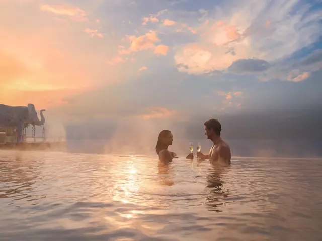 A couple enjoying champagne in a steaming hot spring pool at sunset with a large elephant statue nearby in Kintamani Bali.