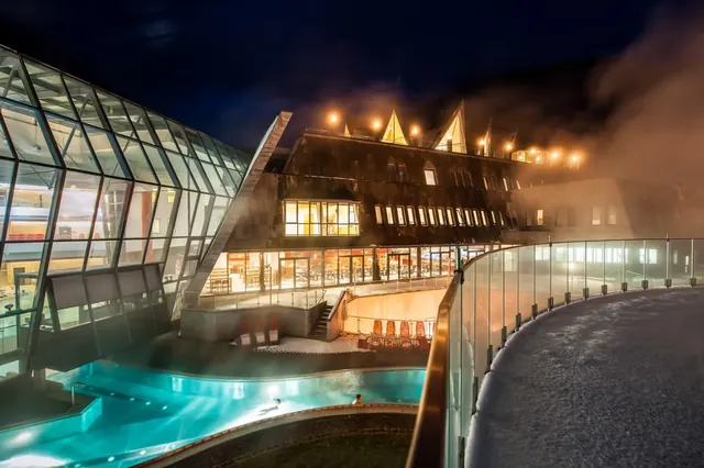 Nighttime scene of steaming outdoor hot spring pools glowing with blue lights at Aqua Dome Tirol Therme near Langenfeld, Austria.