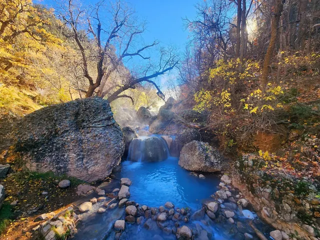 Steamed Fifth Water Hot Springs pool bordered by rocks and autumn trees with yellow leaves near Spanish Fork Utah.