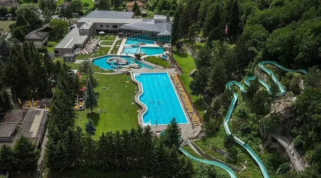 Aerial view of Thermalbad Brigerbad spa showing large outdoor pools and winding water slides amid green forest near Brig Switzerland.