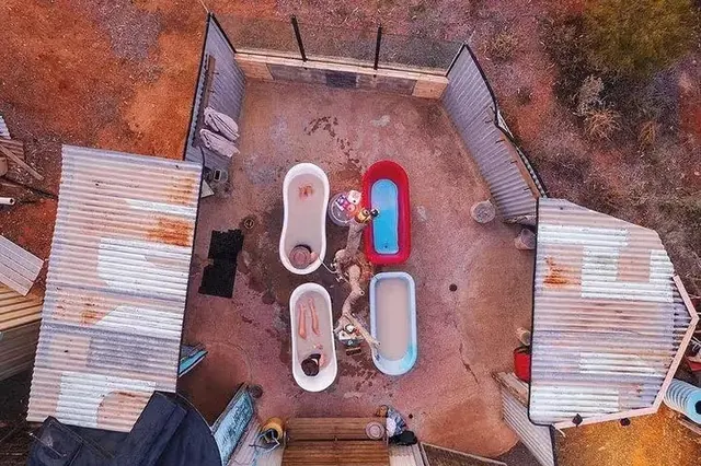 Aerial view of outdoor bathing area with four clawfoot tubs filled with water and people soaking at Eulo Artesian Mud Baths Australia.