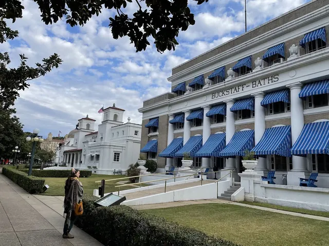 Street view of Buckstaff Bathhouse with blue striped awnings, a pedestrian on sidewalk, and neighboring white buildings in Hot Springs Arka.
