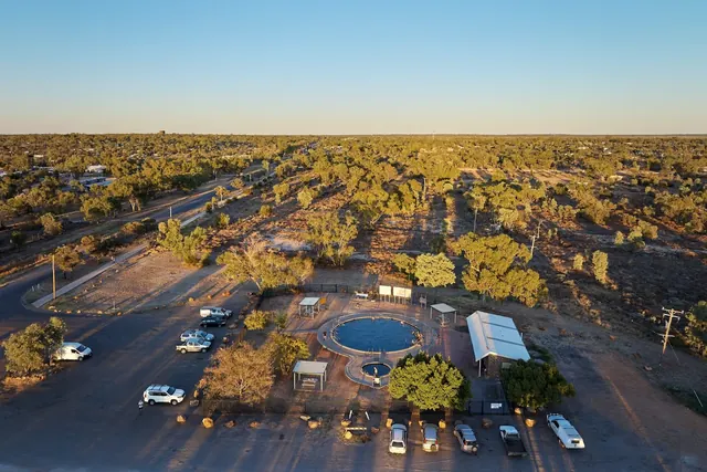 Aerial view of circular hot spring pool surrounded by trees and parked cars at Lightning Ridge Artesian Bore Baths in New South Wales, Aust.