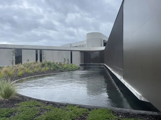 Long curved outdoor pool with dark water alongside modern gray building and landscaped garden at Alba Thermal Springs Australia.