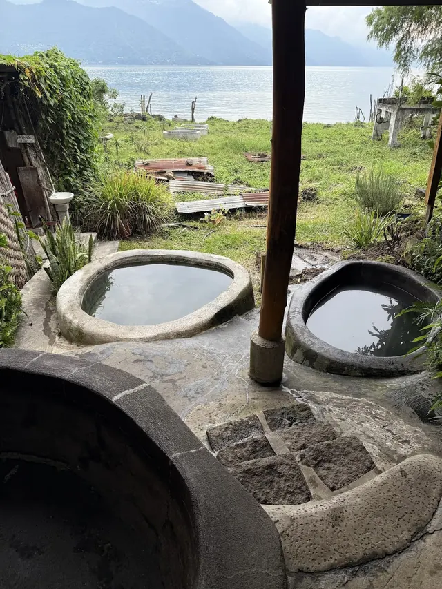 Several stone hot spring pools at Los Termales with a grassy area and Lake Atitlan in the background near San Pedro La Laguna, Guatemala.