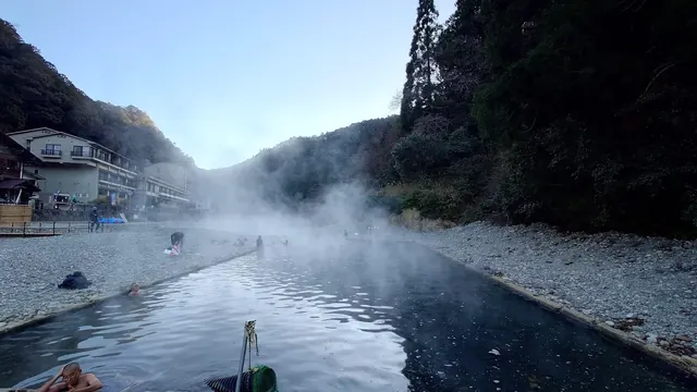 Long outdoor river bath with steam and people soaking beside pebble banks at Kawayu Onsen Sennin-buro near Tanabe city.