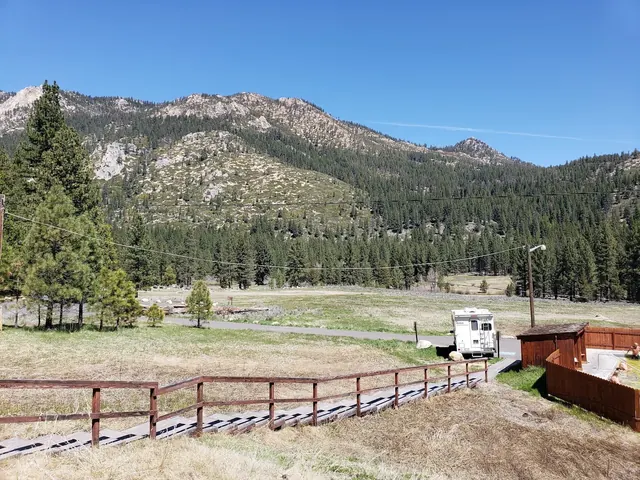 Wooden boardwalk crossing meadow near Grover Hot Springs in Markleeville California with pine trees and rocky hills in the background.